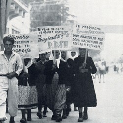 HH129 | Peasant women marching at a political rally in Elbasan: “Forward with the building of a socialist society,” “Let us implement the historic resolutions of the Fourth Congress of the Albanian Party of Labour,” “Let us construct socialism with a pickaxe in one hand and a rifle in the other” (Photo: Harry Hamm 1961).